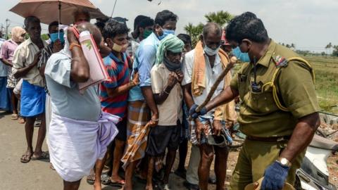 A policeman (R) holding a stick regulates the crowd as people line up to buy alcohol at a liquor shop after the government eased a nationwide lockdown imposed as a preventive measure against the COVID-19 coronavirus, on the outskirts of Chennai on May 7, 2020.
