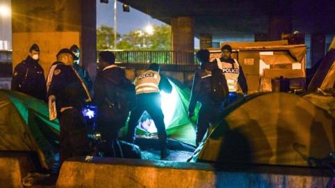 A policeman takes away a baby stroller as migrants are evacuated by the police in Paris on 7 November 2019