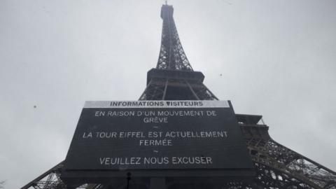This photograph shows a board informing visitors that the Eiffel Tower, viewed in the background, is closed, during a strike of the Eiffel Tower's staff