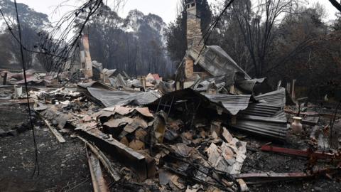 A woodchip mill burnt by bushfires is seen as smoke rises in Eden in Australia's New South Wales state on 6 January, 2020.