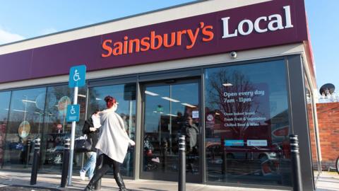 A woman walking into a Sainsbury's local convenience store