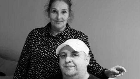 A black-and white picture of Robbie and Shell. She stands behind him wearing a polka dot blouse. Robbie is wearing a white baseball cap.