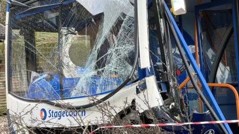 A crashed bus with a smashed windscreen on top of a tree