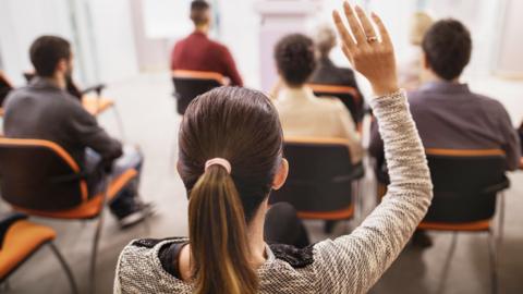 A person in a group holding their hand up to ask a question