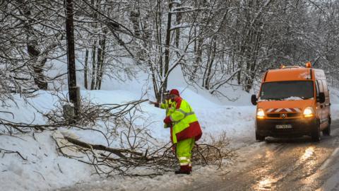 An employee of the Departmental Infrastructure Authority clears fallen tree branches from a road leading to the French Alps ski resorts of Les Menuires and Val Thorens on January 4, 2018
