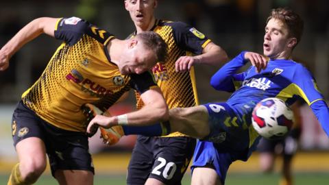 Newport's Cameron Norman battles for the ball with AFC Wimbledon's Jack Currie.