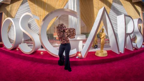 A TV reporter poses beside an Oscars statue on the red carpet area on the eve of the 92nd Oscars ceremony in 2020