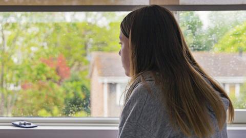 Stock image of a teenage girl looking out of a bedroom window