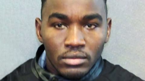 Police mugshot of Badreddin Abdalla Adam Bosh, with dark eyes, eyebrows and thin moustache and small beard on chin. Head and shoulders shot looking straight ahead at camera