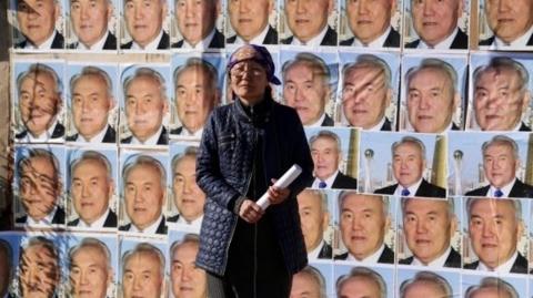 Woman standing outside her home plastered with images of the Kazakh president