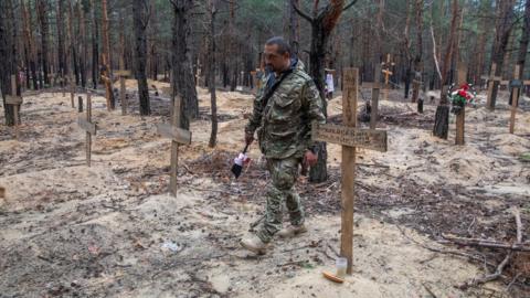 Ukrainian serviceman walks among graves of mostly unidentified civilians and Ukrainian soldiers at an improvised cemetery in the town of Izium