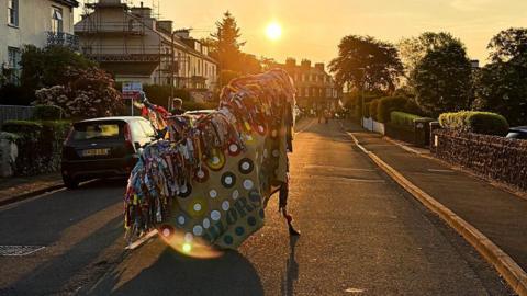 A hobby horse covered in colourful rags dancing down a street in Somerset at dawn, to mark May Day