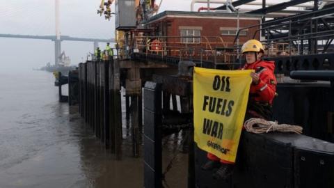 Greenpeace activist with banner that reads foil fuels war