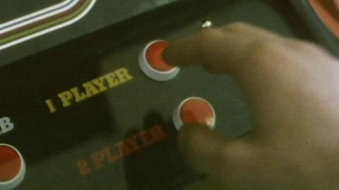 A hand pressing a button on an arcade machine.