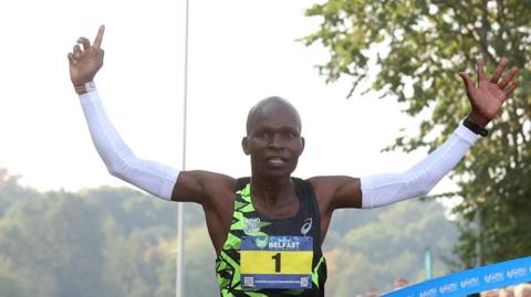 Man crossing finish line at marathon with hands in the air