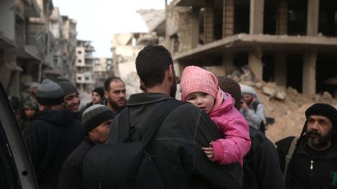 A Syrian child clings on to her father as they prepare to evacuate one of the few remaining rebel-held pockets in Arbin, in Eastern Ghouta, 24 March