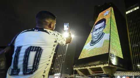 A person takes photos of an image of football icon Pele displayed on a building as a tribute