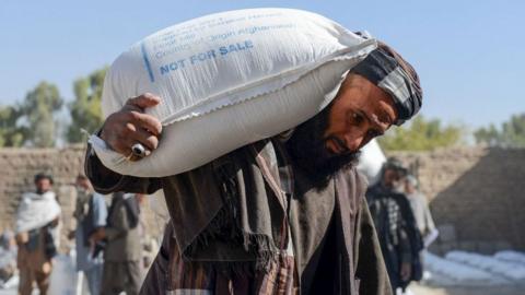 Afghan people carry sacks of food grains distributed as an aid by the World Food Programme (WFP) in Kandahar on October 19, 2021