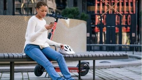 Woman sitting on a bench next to an e-scooter