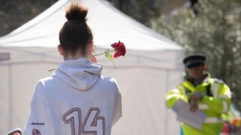 a woman stands with a rose before scene of a crime in London