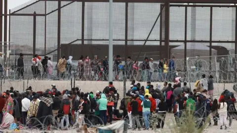 Migrants queue to cross the border into the United States from Ciudad Juarez, Mexico