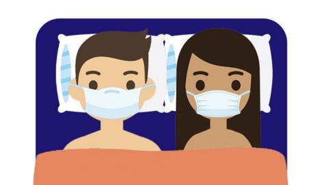 Two people with face masks on in bed