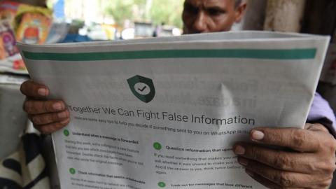 An Indian newspaper vendor reads a newspaper with a full back page advertisement from WhatsApp to counter misinformation.