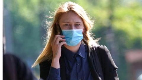 A head and shoulders shot of Lauren Saint George wearing a face mask and holding a phone to her ear.