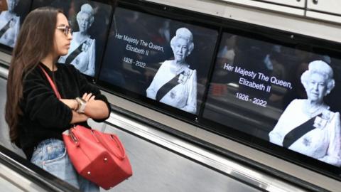 Woman travelling on Tube by images of the Queen