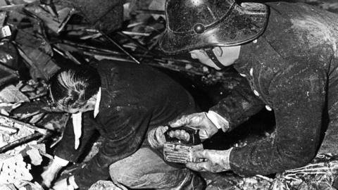 A firefighter holds a torch while a man searches through the rubble of McGurk's bar
