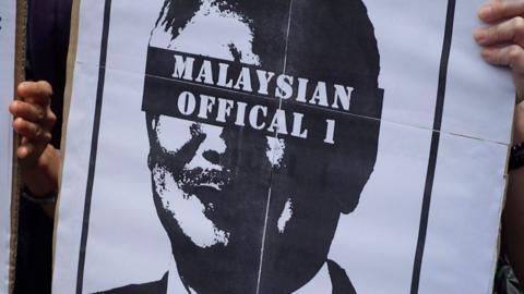 Protester's sign, with an image of Najib Razak with his eyes blacked out by text reading "Malaysian Official 1"