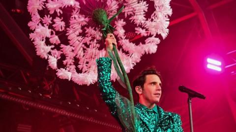 Mike on stage holding a giant flower