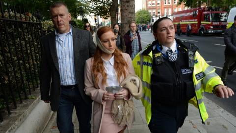 A female casualty is led from the scene by a police officer