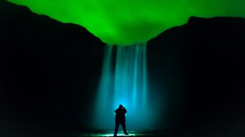 a waterfall is illuminated under the aurora lit sky