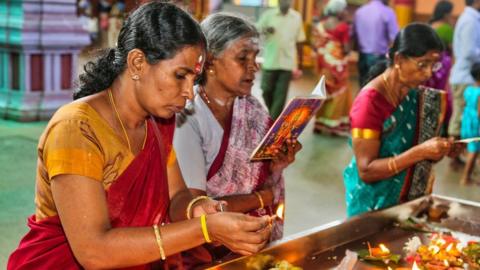 Tamil Hindu women light small lamps while offering prayers at a temple in Matale, Sri Lanka.