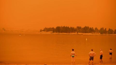 Swimmers stand near the water under a red sky at Jindabyne in New South Wales on 4 January