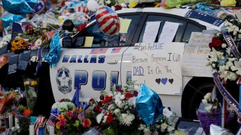 Notes, flowers and other items decorate a squad car at a make-shift memorial in front of the Dallas police department, Saturday, July 9, 2016, in Dallas.