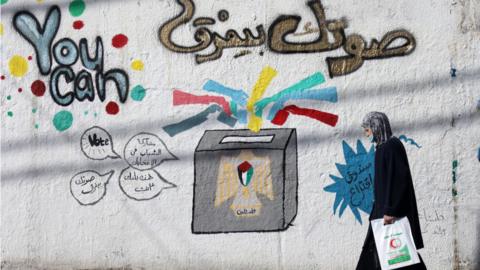 Woman walks past election campaign mural in Gaza City (01/04/21)