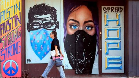 Pedestrians walk past murals painted on boards covering bar windows on 6th Street on May 20, 2020 in Austin, Texas