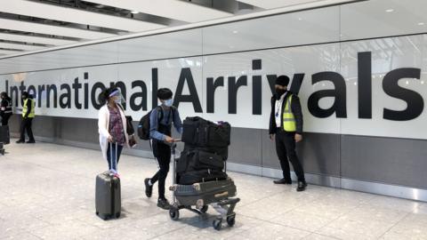 Passengers are escorted through the arrivals area of terminal 5 towards coaches destined for quarantine hotels