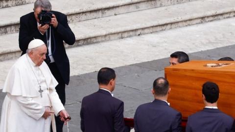 Pope Francis stands as pallbearers carry the coffin of former Pope Benedict