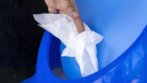 A hand putting a wet wipe into a blue bin