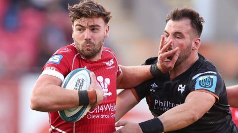 Johnny Williams of Scarlets hands off Scott Baldwin of Ospreys
