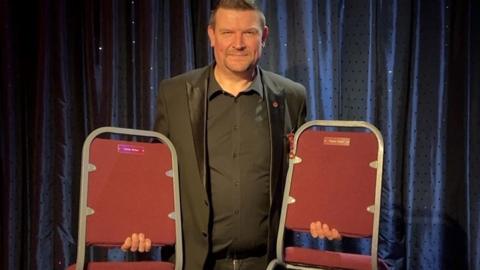 Lee Hathaway of The Magic Circle holding two of the famous chairs