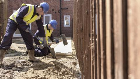 Apprentice builders laying paving stones on building site - stock photo