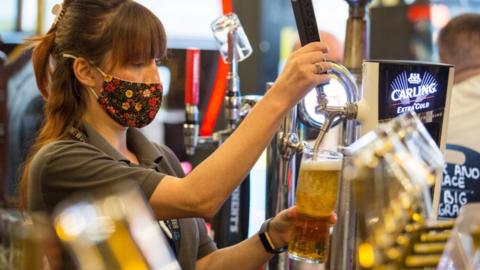 A woman serves a pint in a bar