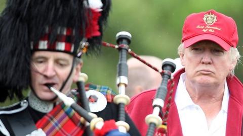 Donald Trump next to a man playing bagpipes at the opening of The Trump International Golf Links Course in July 2012