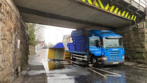 Lorry sat under the bridge as the skips it was carrying lie on the road