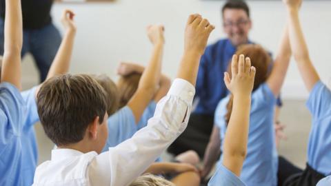 Children with raised hands in a clasroom