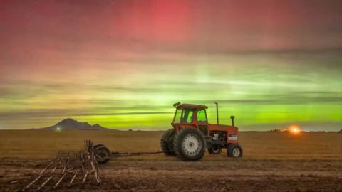 Vivid greens and pinks in the sky over a field with a tractor in the foreground.